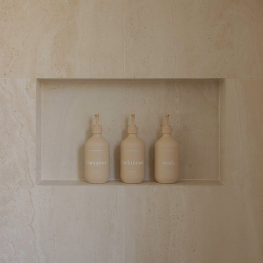 Three bottles wash shampoo conditioner in a recessed shelf against a beige stone wall.