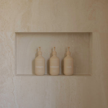 Three bottles wash shampoo conditioner  in a recessed shelf against a beige stone wall.