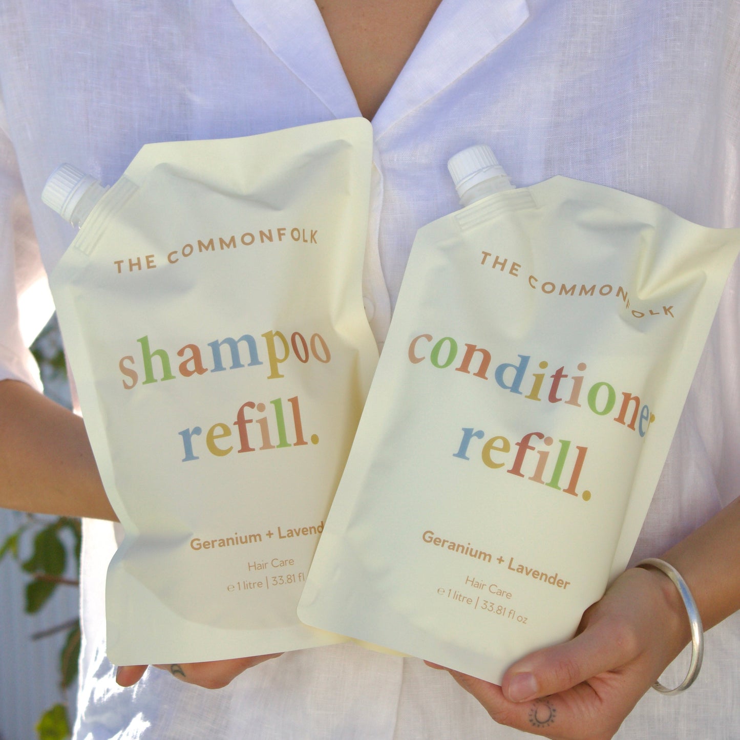Person holding The Common Good shampoo and conditioner refill packs.