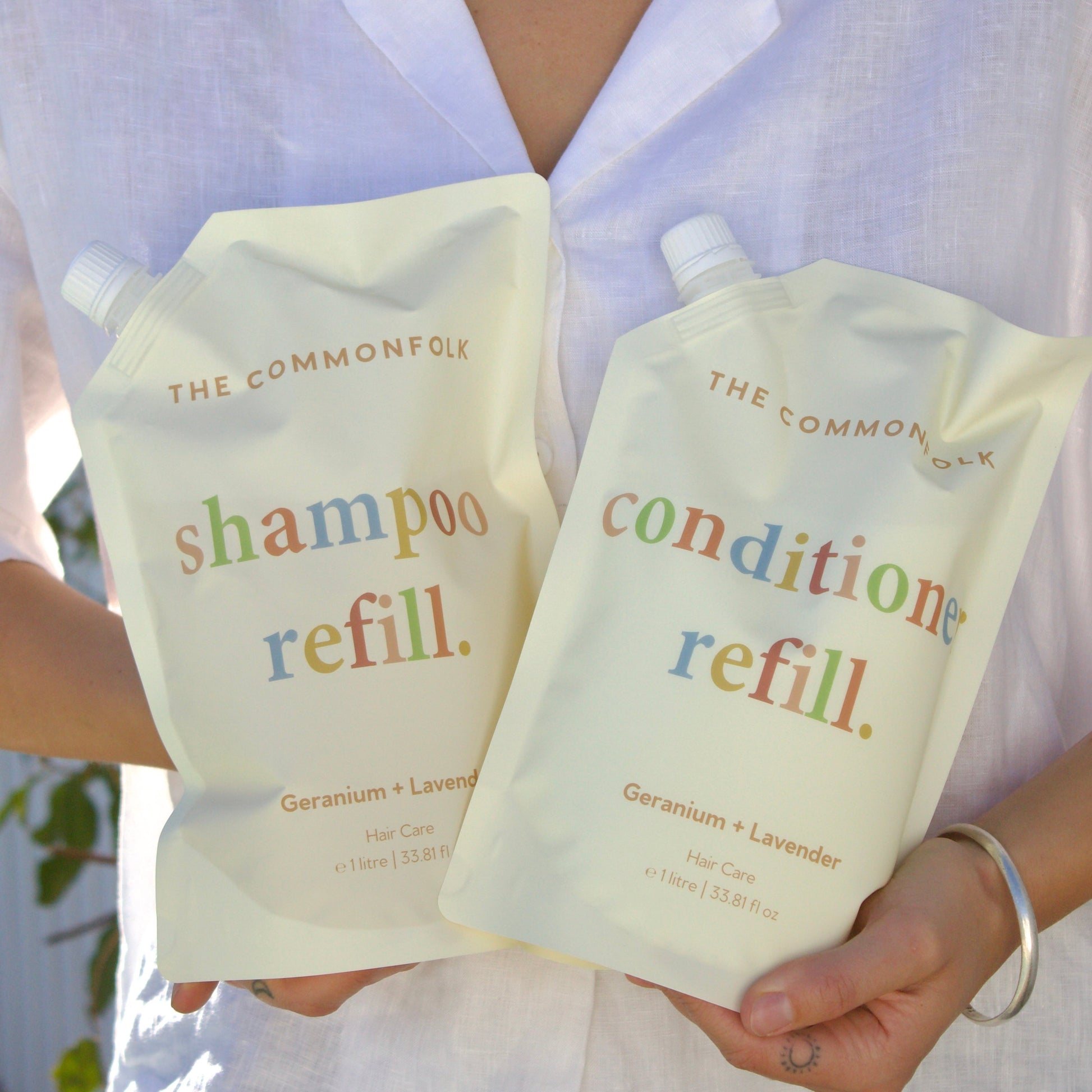 Person holding The Common Good shampoo and conditioner refill packs.
