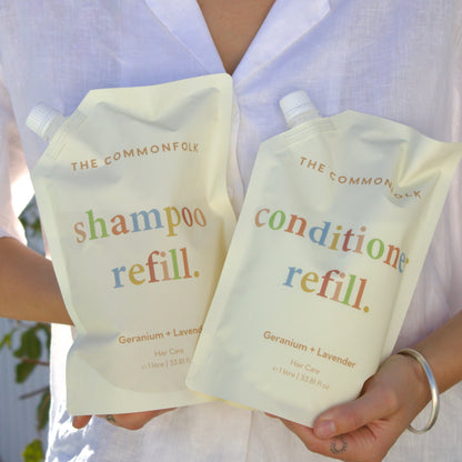 Person holding The Common Good shampoo and conditioner refill packs.