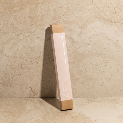 The Commonfolk scented incense ritual sticks pack, with a pink body and brown tip, stands upright against a textured beige background.