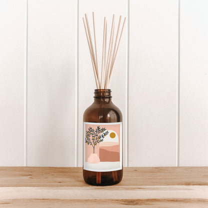 The Commonfolk room diffuser with natural bamboo reed sticks in a brown bottle features a label with an illustration of a tree and the sun.
