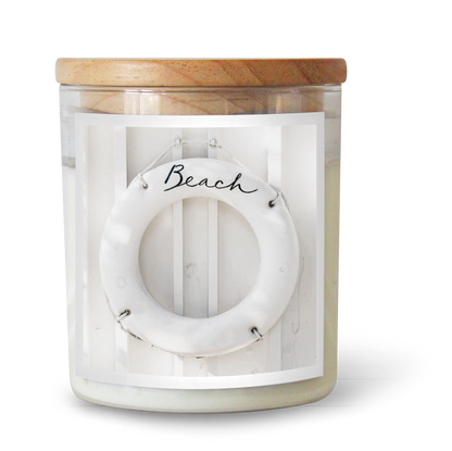 The Commonfolk scented white candle, with a label featuring the word 'Beach' and a circular design, is topped with a natural wood lid.