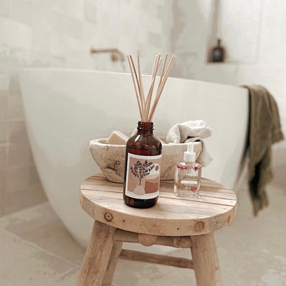 A wooden stool holding a bottle of room diffuser and a neatly folded towel.