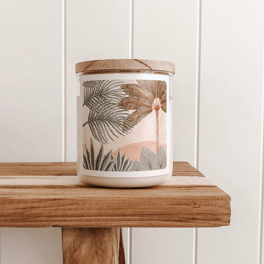 A candle on a wooden shelf, surrounded by palm trees, creating a serene and tropical atmosphere.
