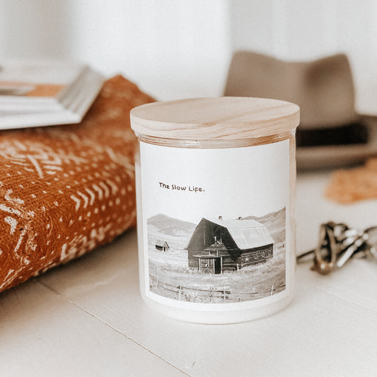 A candle on a table beside a book and a hat, creating a cozy and inviting atmosphere.