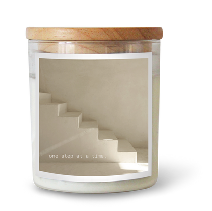 The Commonfolk scented candle with a white label, features a staircase design and the text 'one step at a time'.