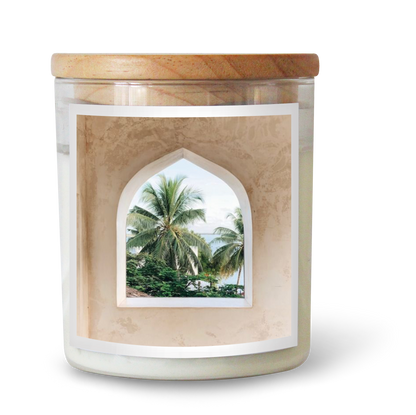 The Commonfolk scented candle features white wax and a window-like design on the label showcasing a tropical scene with palm trees.