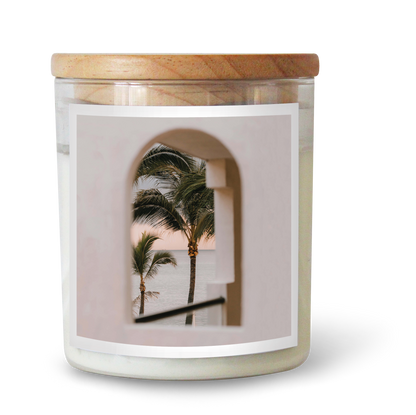 The Commonfolk scented candle, with a white label featuring an image of palm trees, is topped with a wooden lid.