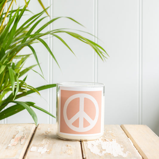 A peace sign candle on a wooden table beside a green plant, creating a serene and calming atmosphere.