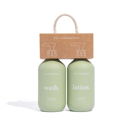 The Commonfolk two matte sage green finish bottles labeled 'wash' and 'lotion', respectively, with a recycled Kraft carry caddy on top featuring a rope handle.