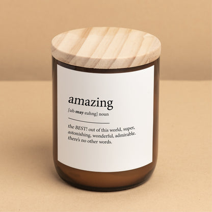 The Commonfolk scented candle with a white label that defines the word 'amazing,' placed on a brown jar with a wooden lid.